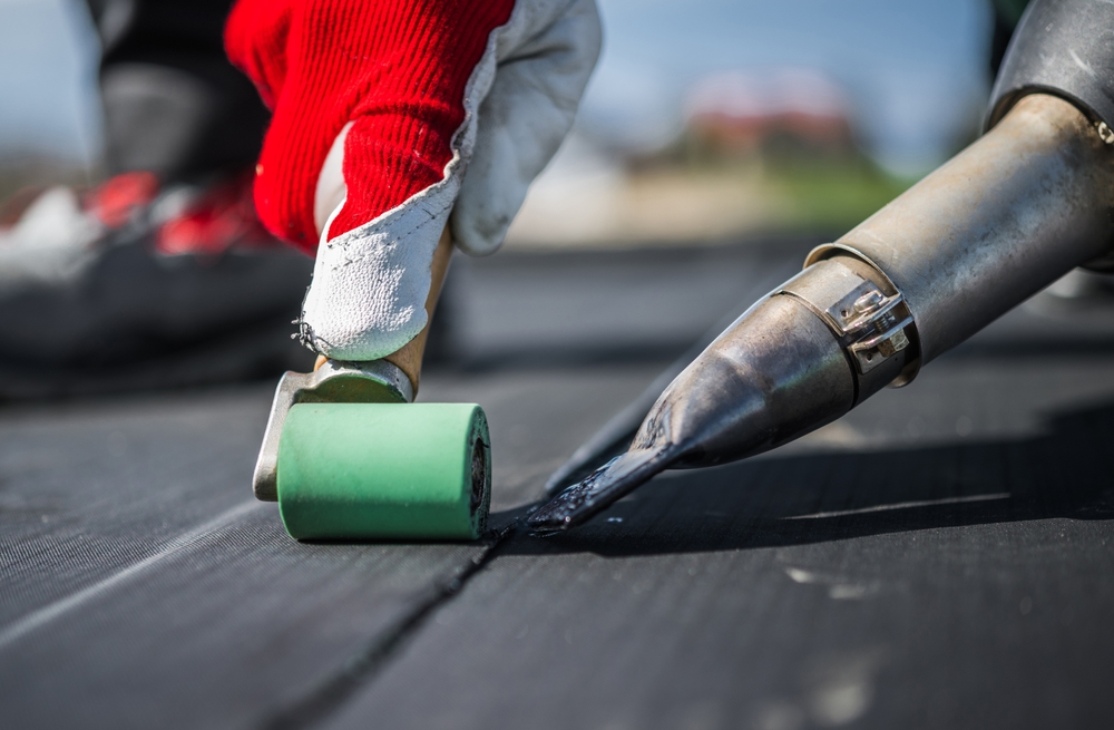 Roof worker attaching pieces of EPDM membrane roofing material using a hot air blower and industrial roller