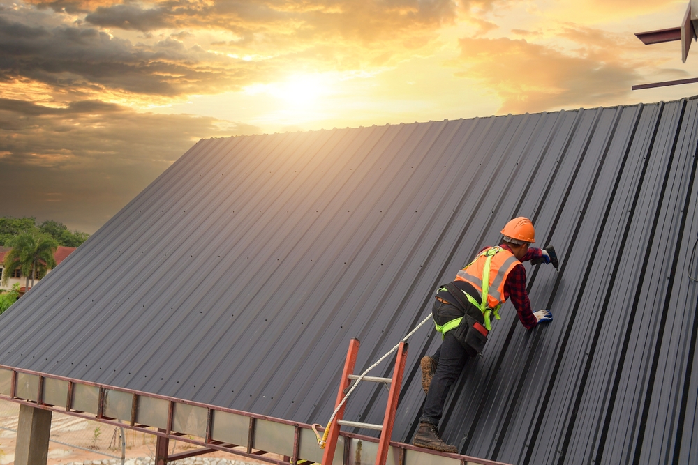  Construction worker wearing a safety harness belt while working on the roof of a building, using a pneumatic nail gun
