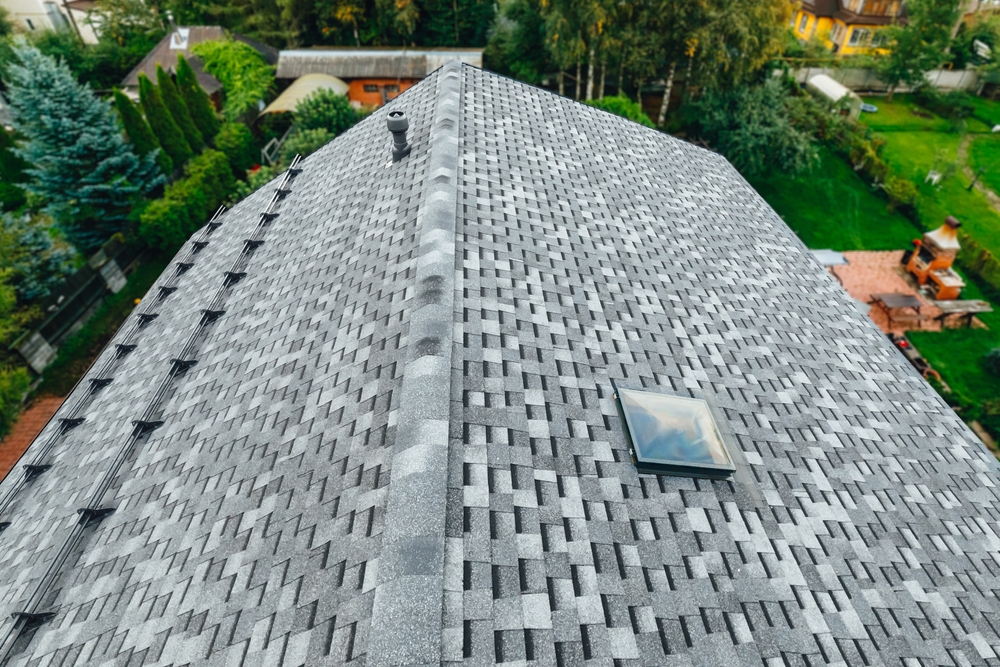 Roof of a new house featuring shingles, roof tiles, a ventilation window, and a snow retention system